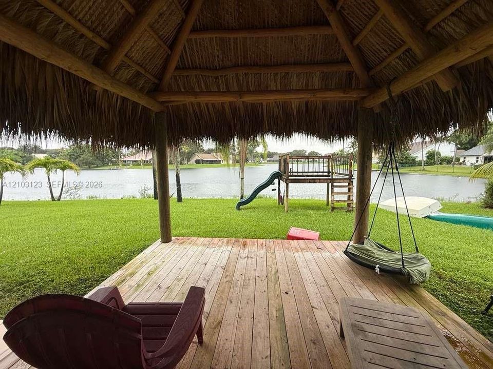 Thatched-roof tiki hut featuring exposed timber beams, wood-plank decking, and water frontage