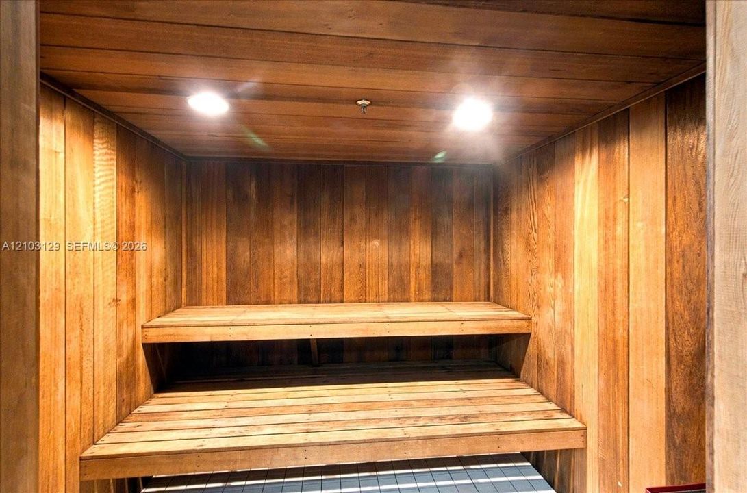 Sauna featuring natural wood wall paneling, tiered built-in wood bench seating, and recessed ceiling lighting