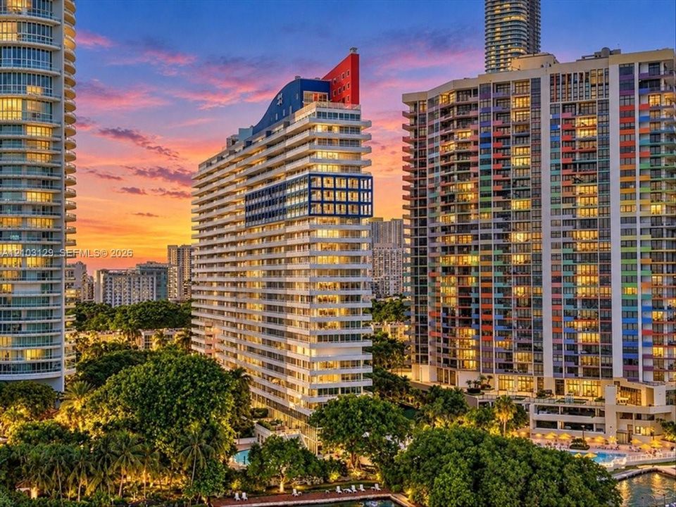 High-rise residential tower featuring architectural geometric detailing, balcony facades, and a vibrant sunset backdrop