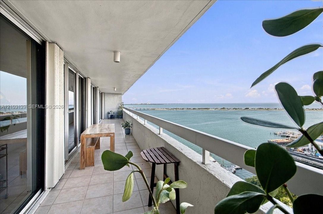 Expansive covered balcony featuring tile flooring, a concrete ceiling with integrated lighting, and a metal railing overlooking the water