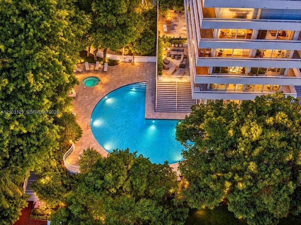 Multi-level building exterior featuring a crescent-shaped swimming pool, built-in spa, stone-finish pool deck, and mature landscaping