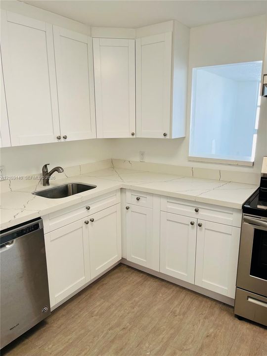 Kitchen featuring white Shaker-style cabinetry, quartz countertops with integrated backsplash, stainless steel appliances, and wood-finish flooring