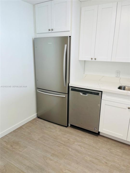 Kitchen featuring white shaker-style cabinetry, stainless steel refrigerator and dishwasher, stone-finish countertops, and wood-finish flooring