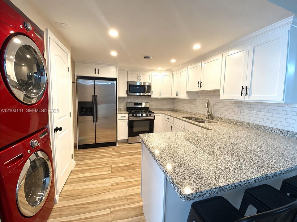 Kitchen featuring white cabinetry, stone-finish countertops, subway tile backsplash, stainless steel appliances, and wood-finish flooring