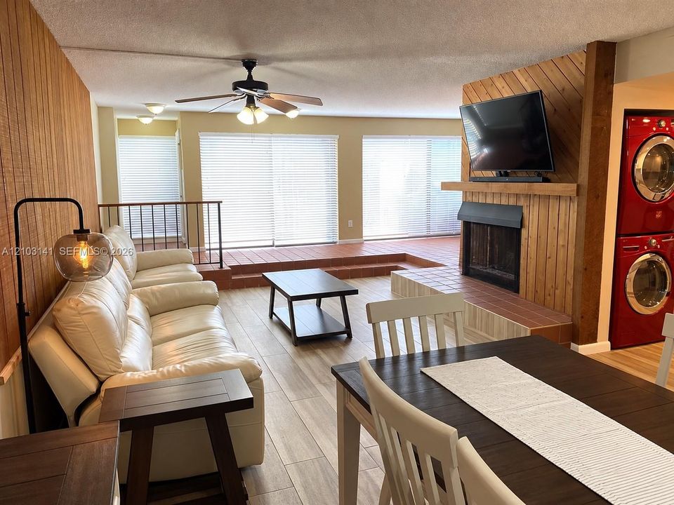 Living space featuring wood-paneled accent walls, a floor-to-ceiling fireplace with a tile hearth, tile flooring, and integrated laundry appliances