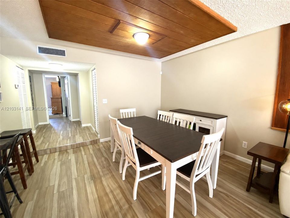 Wood-finish flooring throughout, recessed ceiling detail with natural wood-grain paneling, and louvered closet doors
