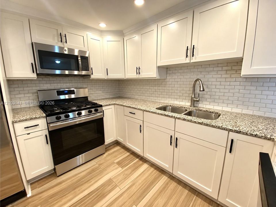 Kitchen featuring white shaker-style cabinetry, speckled stone countertops, a subway tile backsplash, stainless steel gas range with built-in microwave, and wood-finish flooring