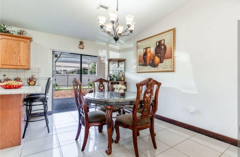 Dining area featuring large-format tile flooring, a multi-arm chandelier with glass shades, wood cabinetry, a tiled backsplash, and sliding glass doors