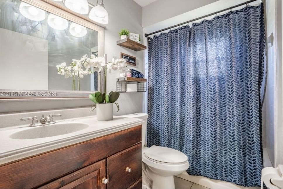 Bathroom vanity featuring wood-finish cabinetry, a light-toned integrated countertop, a wide-frame wall mirror, and dual wall-mounted floating wood shelves