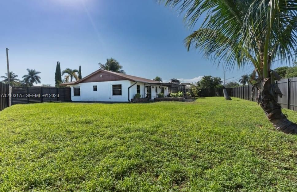 Expansive backyard featuring a level lawn, mature palm trees, stone-accented hardscaping, and full perimeter privacy fencing