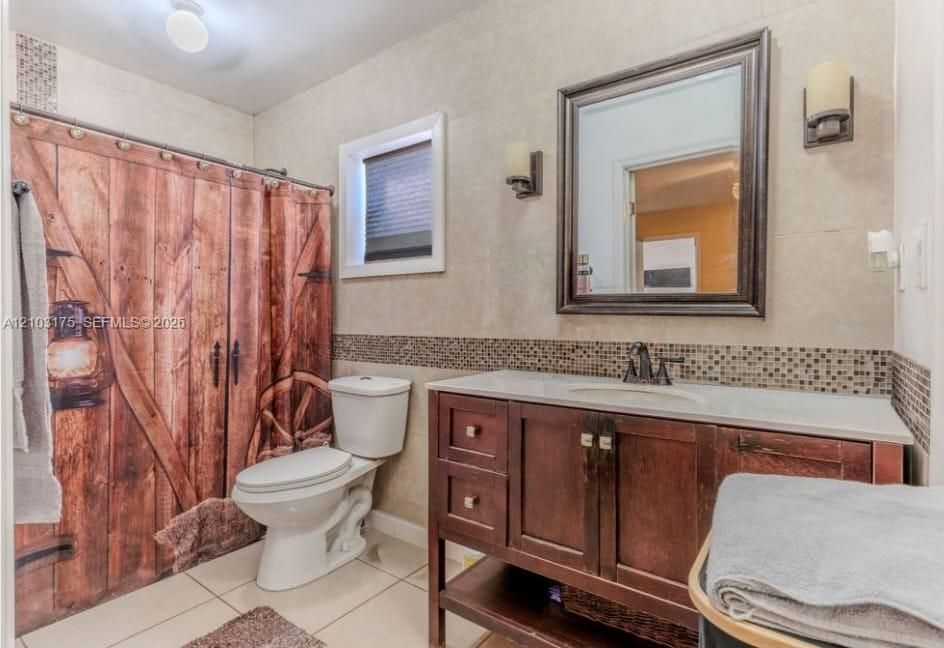 Bathroom featuring a dark wood vanity with a stone-finish countertop, dual wall-mounted light fixtures, framed vanity mirror, and neutral wall tiling with a mosaic accent border