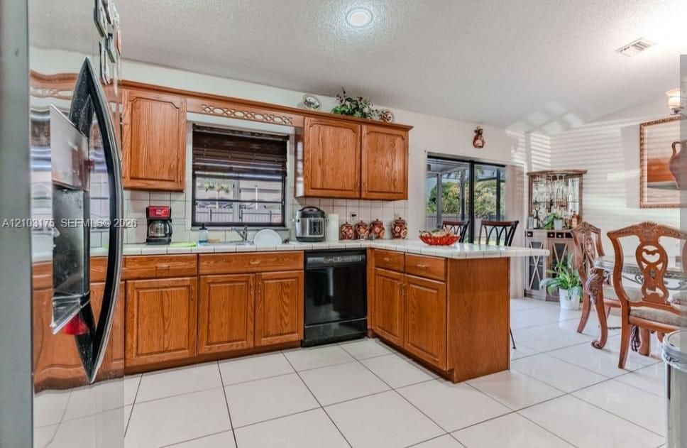 Kitchen featuring wood cabinetry, tile countertops, tile flooring, and integrated black appliances