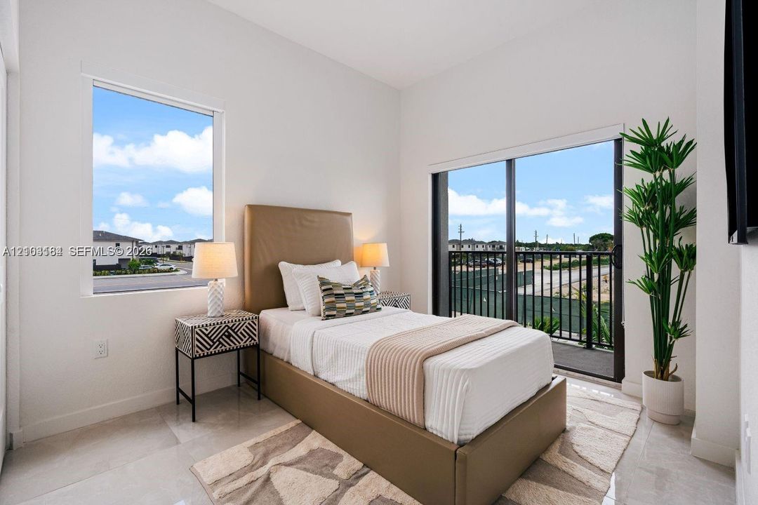 Neutral-toned room featuring high ceilings, light-colored tile flooring, oversized windows, and a sliding glass door providing access to a private balcony with metal railings