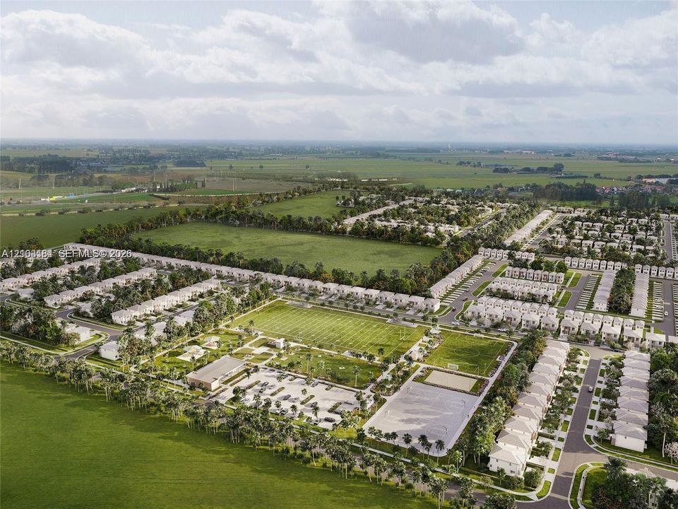 Aerial perspective of a residential development featuring expansive green spaces, multiple athletic fields, paved parking areas, and mature landscaping