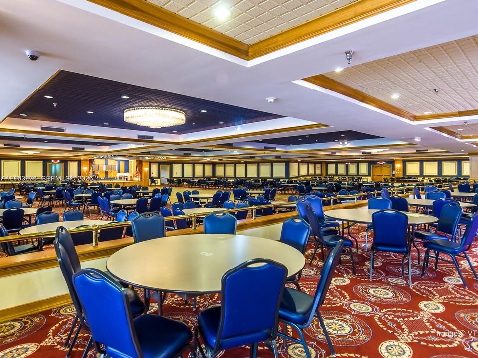 Large gathering space featuring a tiered coffered ceiling, recessed accent lighting, a central tiered chandelier, and patterned wall-to-wall carpeting