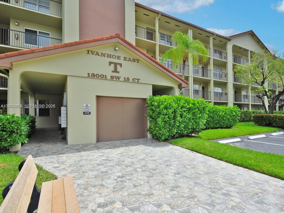 Multi-story building exterior featuring a tiled roof entry, paver stone walkway, and structured landscaping