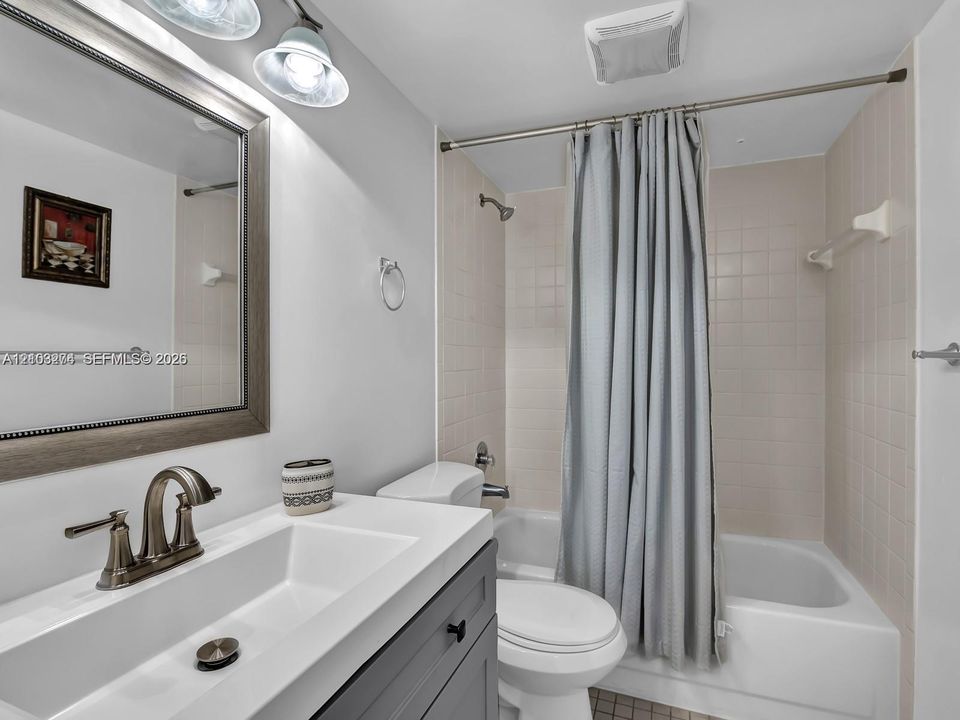 Bathroom featuring a dark gray vanity with a rectangular integrated sink, brushed-metal widespread faucet, framed wall mirror, and tub-shower combination with tiled surround