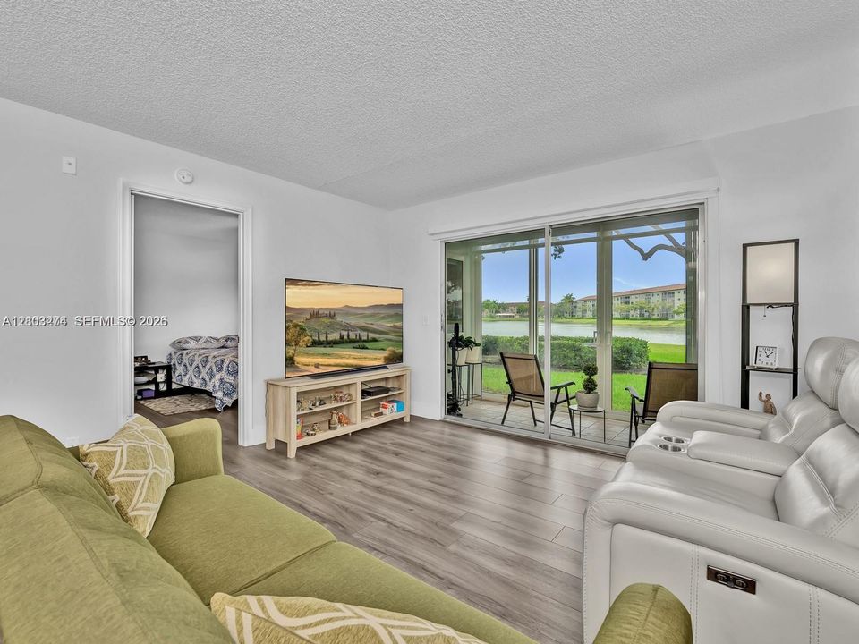 Living area featuring wood-finish flooring, sliding glass doors, and a screened-in patio overlooking a lake