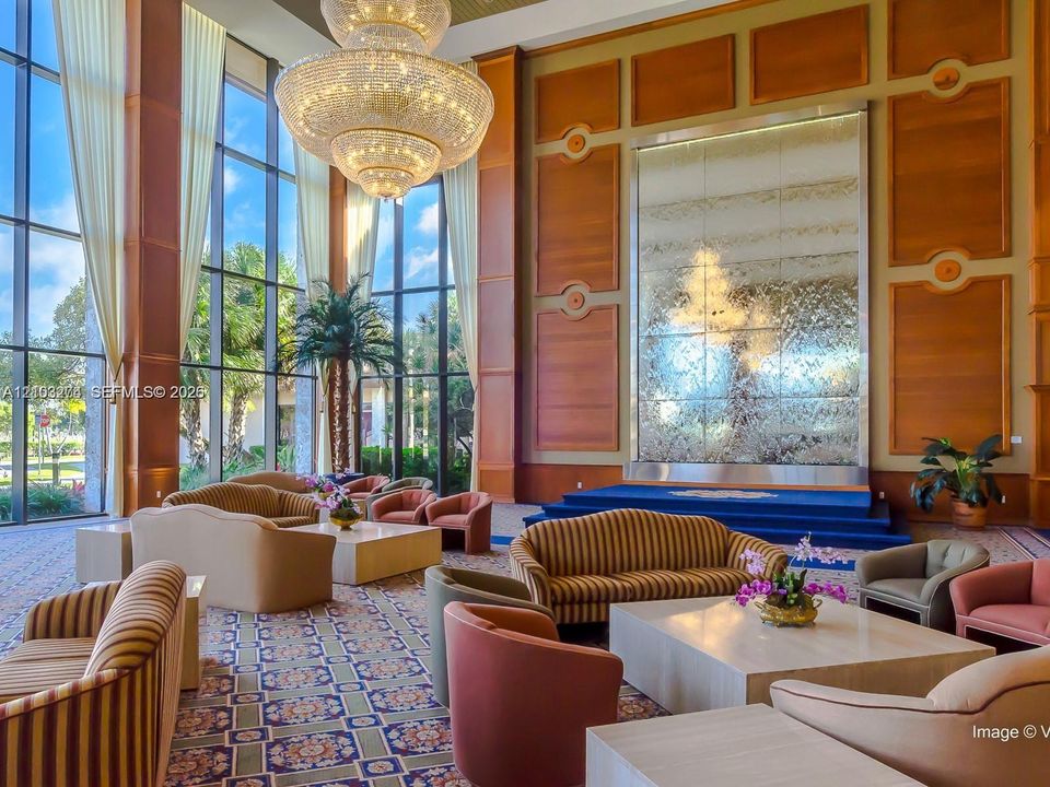 Double-height floor-to-ceiling windows, large-scale crystal chandelier, decorative wood paneling, and an integrated tiered water feature