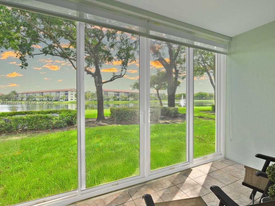 Enclosed porch featuring expansive floor-to-ceiling sliding glass doors, ceramic tile flooring, and a backdrop of waterfront scenery with mature trees