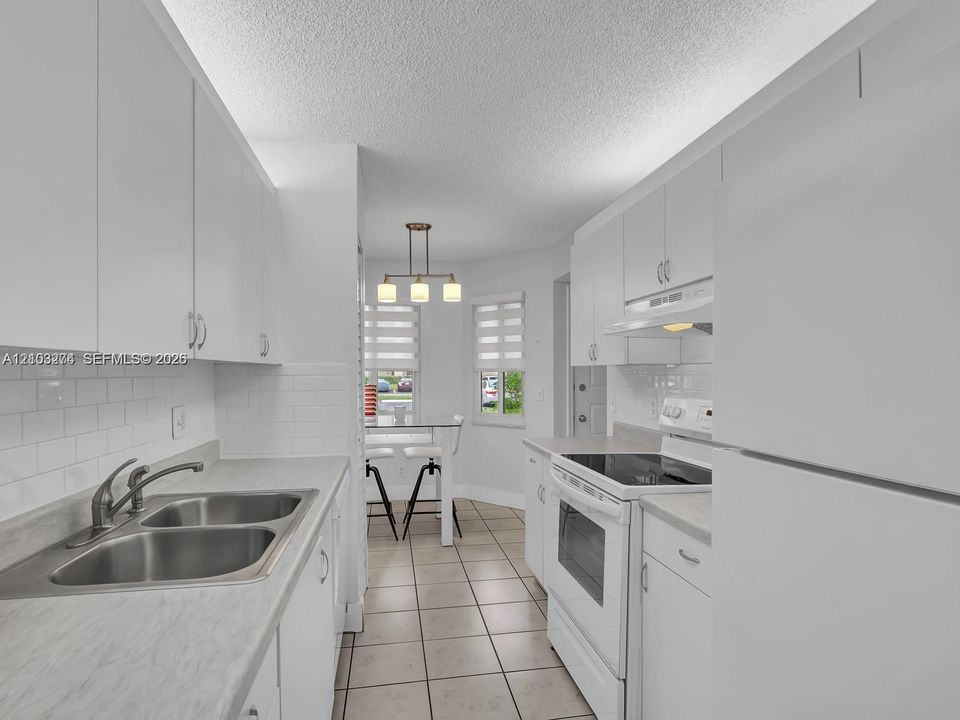 Kitchen featuring white cabinetry, light-toned countertops, tile backsplash, tile flooring, and integrated pendant lighting