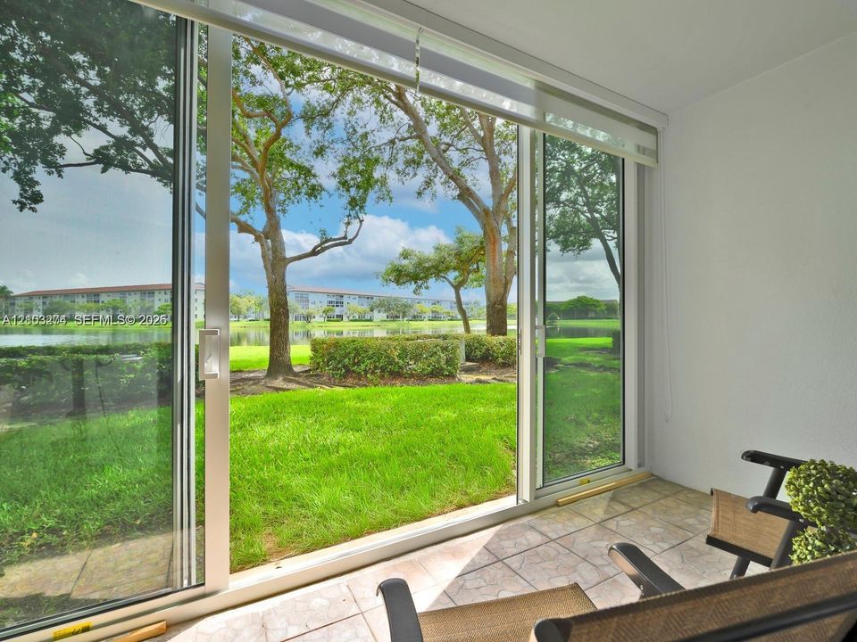 Enclosed patio featuring large glass sliding doors, ceramic tile flooring, and direct exterior access to a lawn and pond