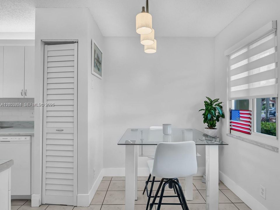 Bright kitchen featuring ceramic tile flooring, three-light pendant fixture, white cabinetry, and horizontal window shade