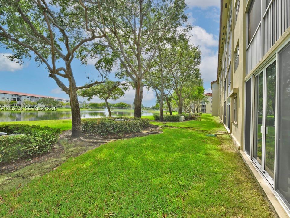 Ground-level exterior featuring a grassy common area, mature shade trees, and a pond with a water feature