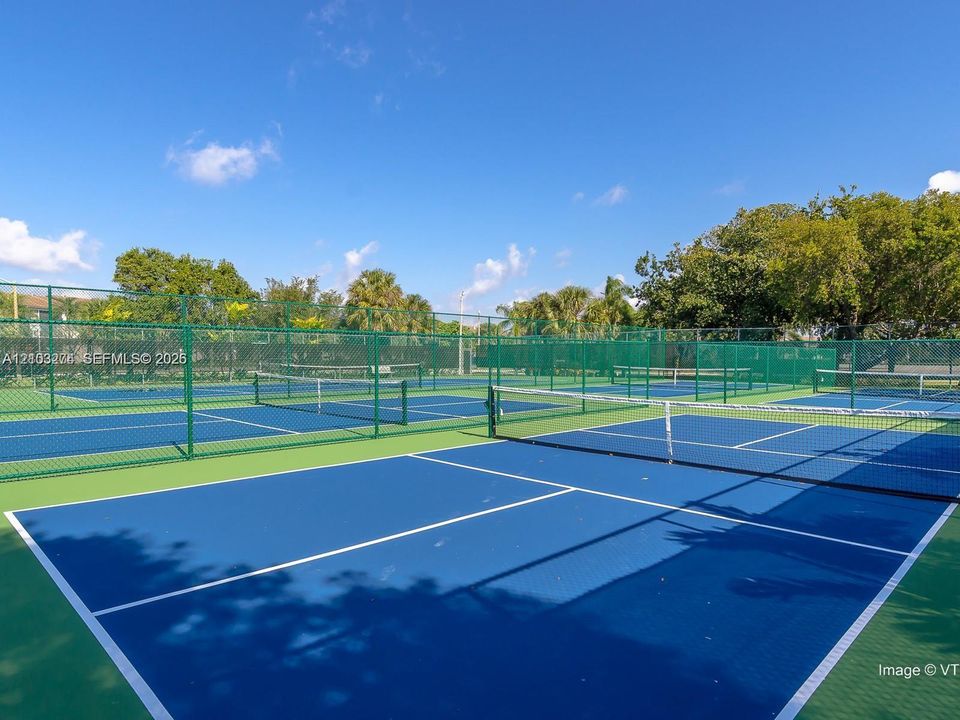 Multi-court tennis facility featuring blue and green acrylic surfaces and perimeter chain-link fencing