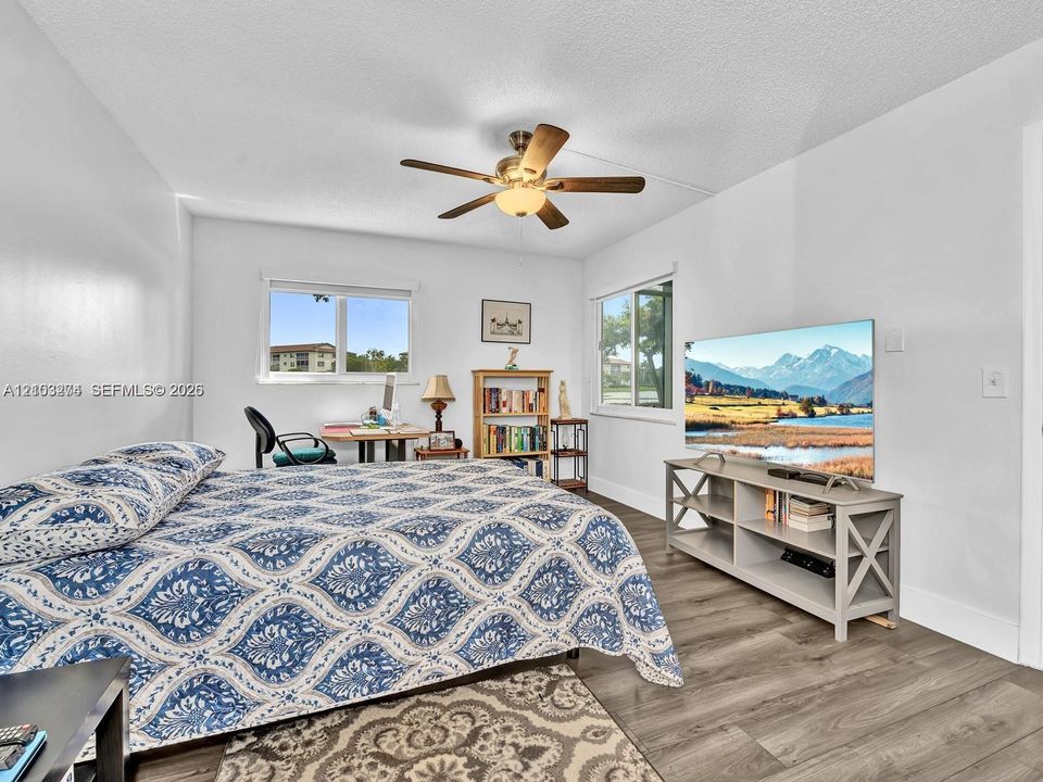 Bedroom featuring wood-finish flooring, dual windows, and a ceiling fan with integrated light fixture