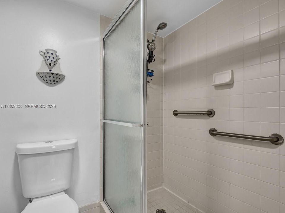 Shower enclosure featuring a glass door, wall-mounted shower head, built-in soap dish, and horizontal grab bars finished in a metallic tone, complemented by neutral ceramic tile wall surfacing