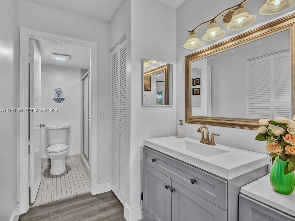Gray vanity cabinet with a white countertop, metallic faucet, framed wall mirror, three-light fixture, and louvered-style closet doors