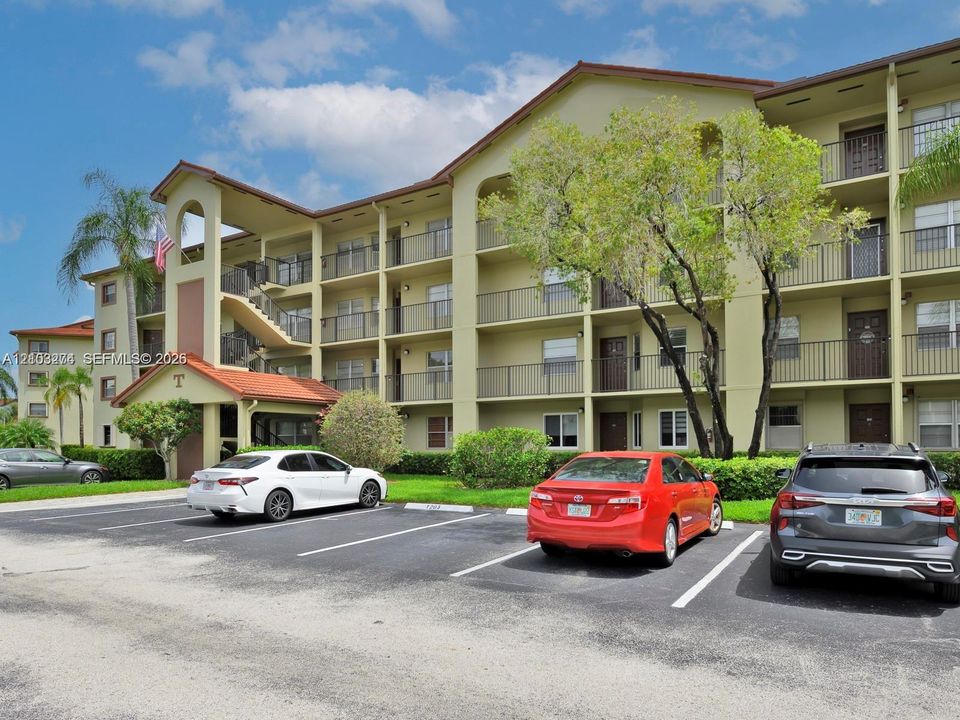 Multi-story residential building featuring stucco exterior, arched architectural detailing, private balconies with metal railings, and tiled roof accents