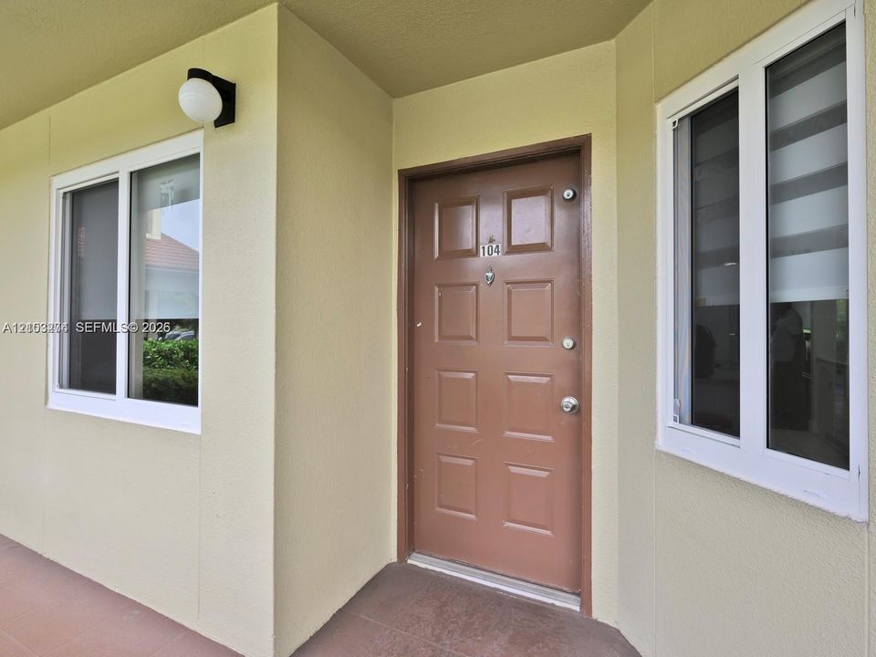 Exterior entryway featuring a six-panel door with metal hardware, dual-pane white-framed windows, and a wall-mounted globe light fixture