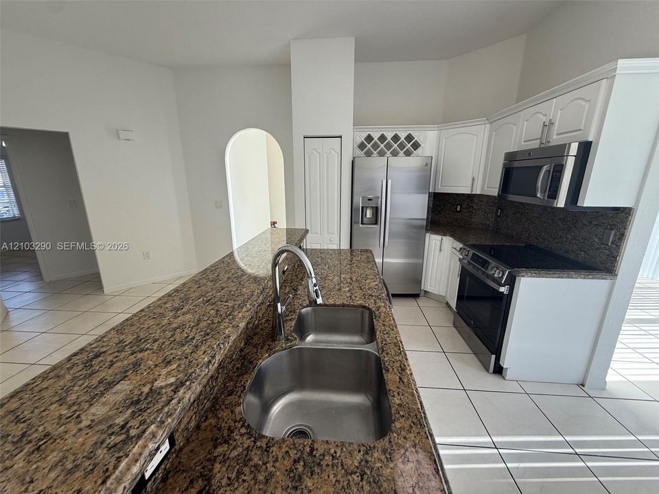 Kitchen featuring white cabinetry with integrated wine rack, stone countertops, stainless steel appliances, double-basin sink with high-arc faucet, and tiled flooring