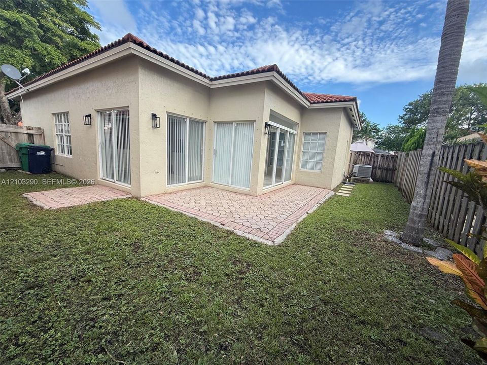 Stucco exterior featuring a red tile roof, multiple sliding glass doors, and an expansive paver patio