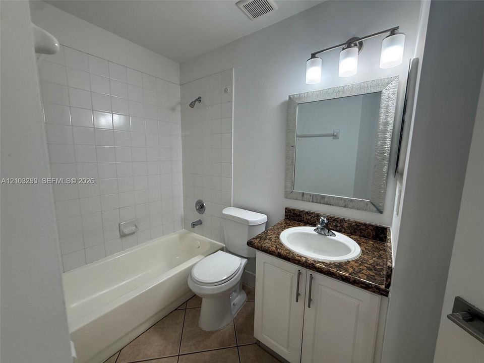 Bathroom featuring a white vanity cabinet, stone-finish countertop, oval undermount sink, three-light fixture, and tub-shower combination with tiled surround