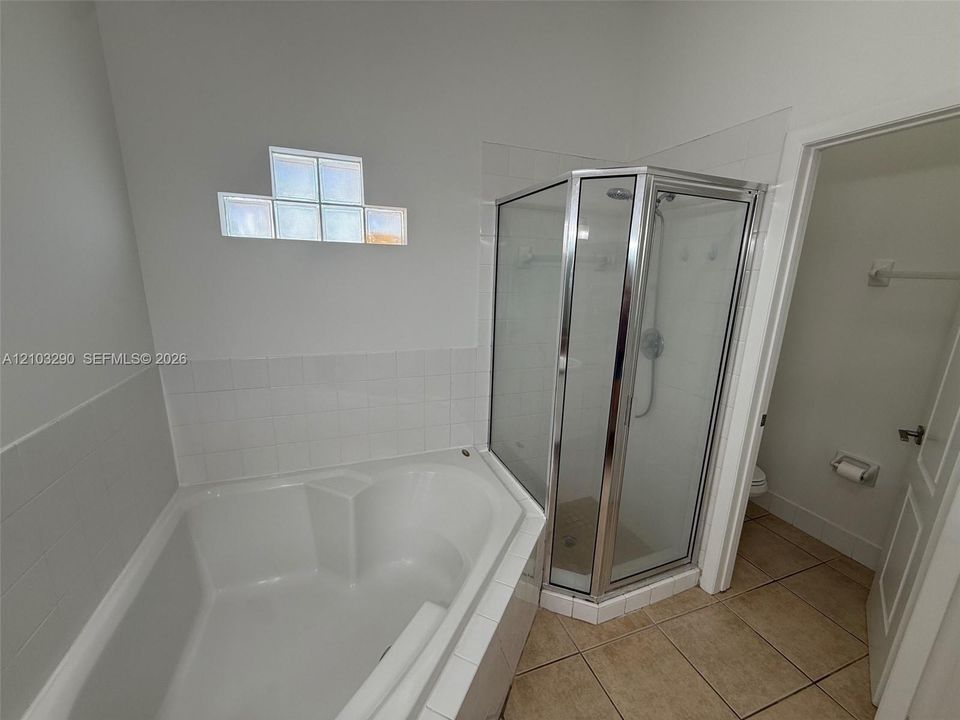 Corner soaking tub with tile surround, glass-enclosed corner shower with chrome hardware, glass block accent window, and ceramic tile flooring