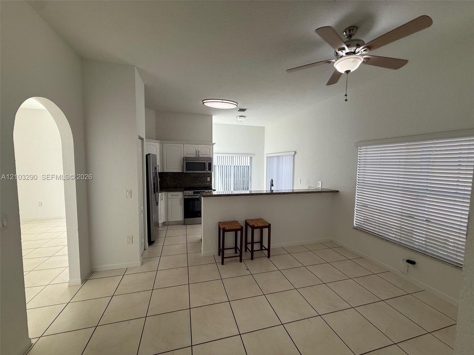 Kitchen featuring white cabinetry, stone-finish countertops, stainless steel appliances, ceramic tile flooring, and a breakfast bar