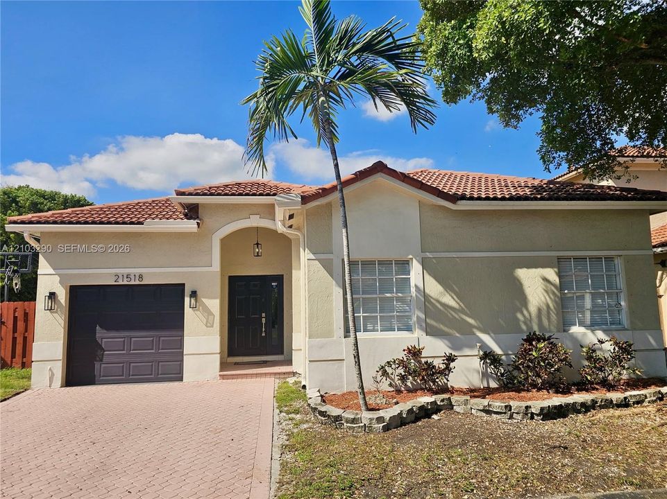 Stucco exterior featuring a red tile roof, arched entryway, paved driveway, and grid-patterned windows