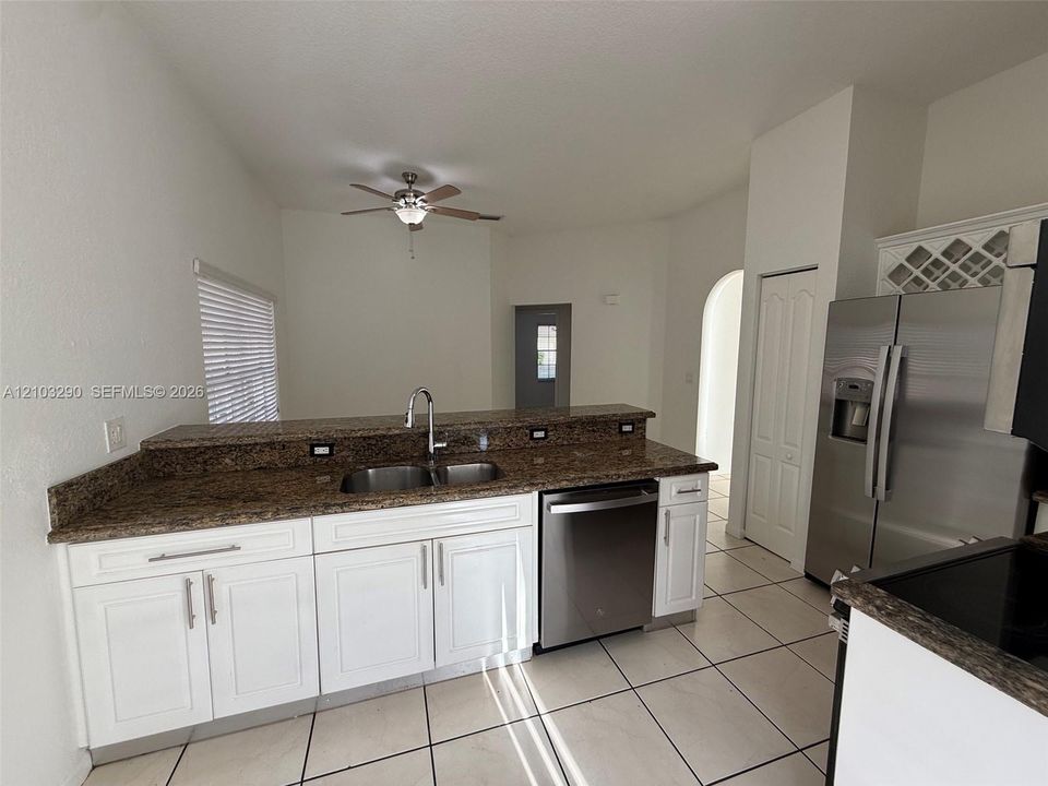 Kitchen featuring white cabinetry, stone-surface countertops, stainless steel appliances, double-basin undermount sink, and tiled flooring