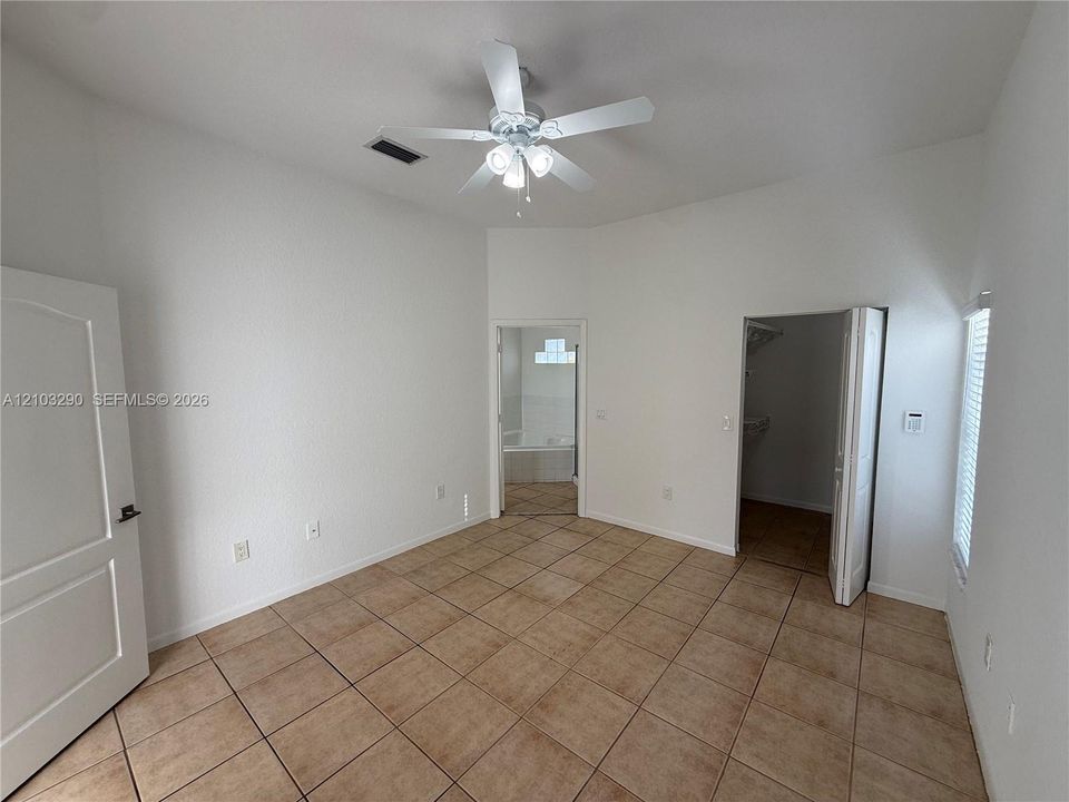 Vaulted ceilings, ceramic tile flooring, ceiling fan with light fixture, and walk-in closet with bi-fold doors