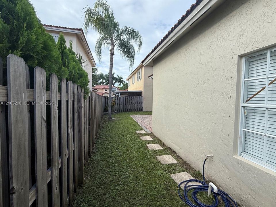 Side yard featuring a paver stone path, lawn, vertical wood fencing, and mature landscaping