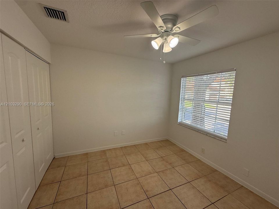 Room featuring neutral-toned tile flooring, dual-panel closet doors, a multi-light ceiling fan, and a window with horizontal blinds