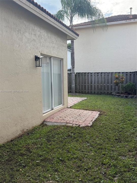 Rear exterior featuring a stucco facade, sliding glass door, paved brick patio, and privacy fencing