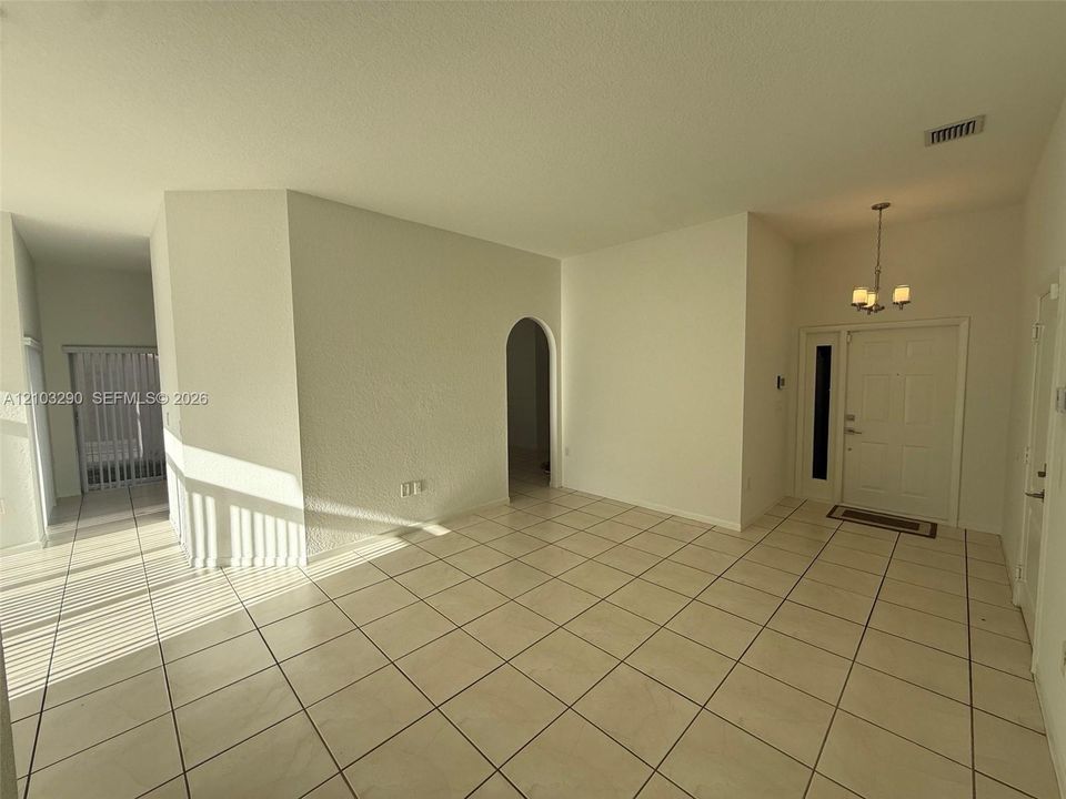 Ceramic tile flooring, arched wall opening, front entry door with a sidelight, and a decorative multi-light ceiling fixture