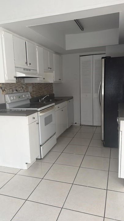 Kitchen featuring white cabinetry, solid-surface countertops, tile flooring, a mosaic tile backsplash, and bifold closet doors