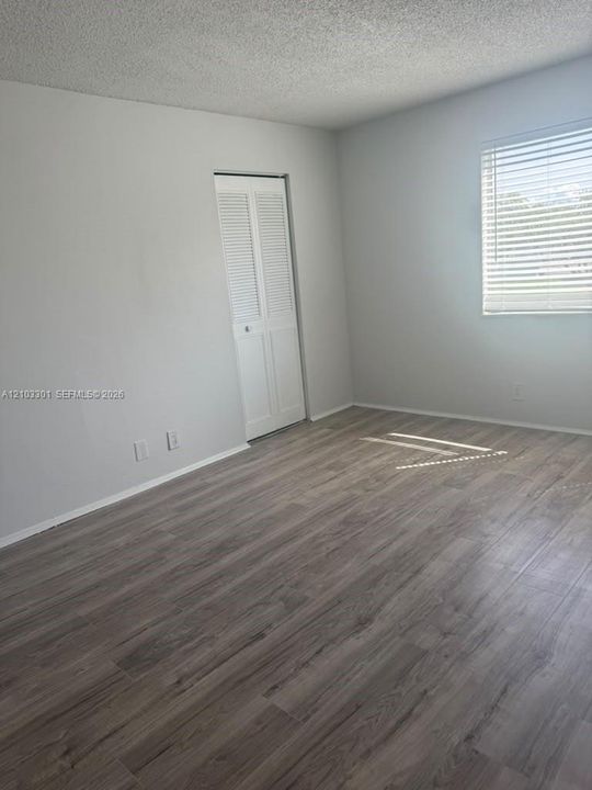 Neutral interior space featuring wood-finish flooring, crisp white walls, a closet with white louvered doors, and a window fitted with adjustable horizontal blinds