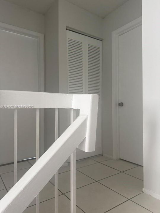 White-painted wood stair railing with vertical balusters, complemented by tile flooring and louvered closet doors