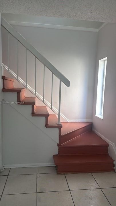 Staircase featuring painted wood-finish treads, a white metal handrail, and a vertical window